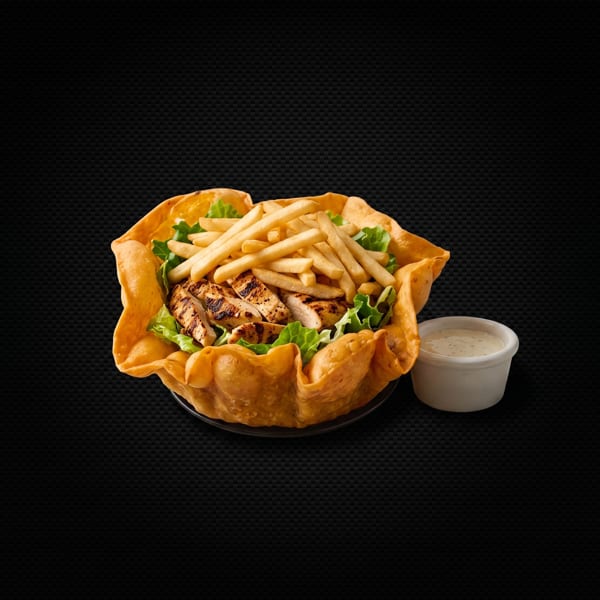Grilled chicken and french fries in a taco shell bowl with a side of ranch dressing.