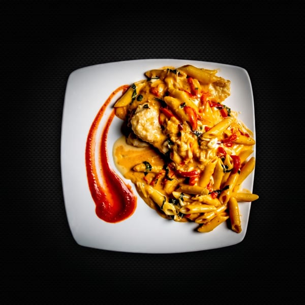 Penne pasta with creamy orange sauce, red peppers, and basil, served on a white plate.