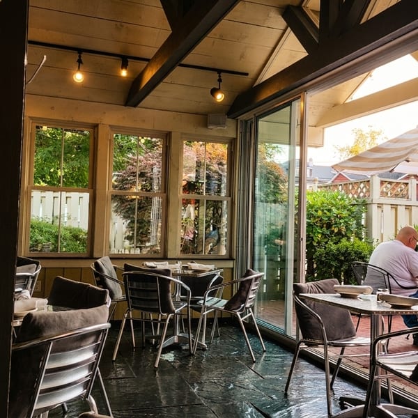 Indoor and outdoor dining areas with patrons, tables, chairs, and a striped umbrella.