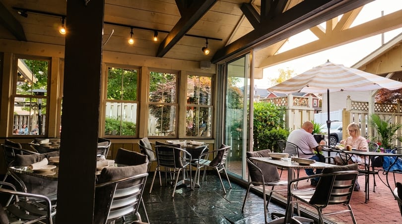Indoor dining area with tables and chairs, and an outdoor patio with people dining under an umbrella.