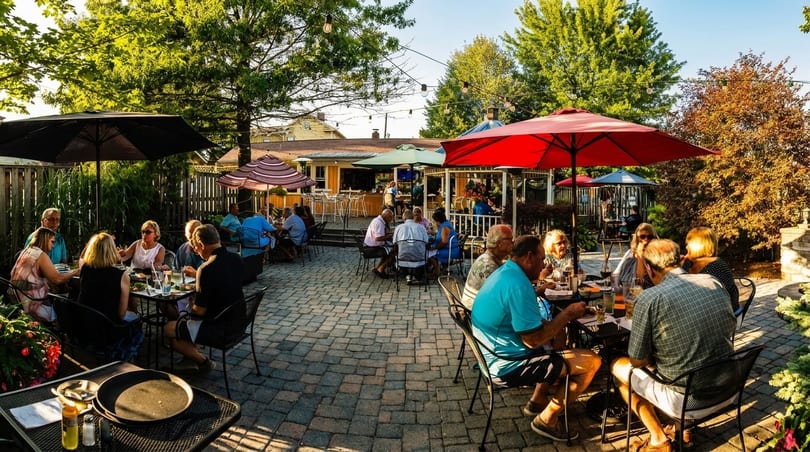 Patrons dine al fresco on a spacious, shaded restaurant patio with string lights and lush greenery.
