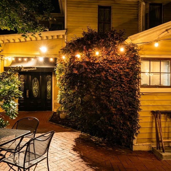 Benjamin's restaurant exterior at night, with string lights, outdoor seating, and a brick patio.