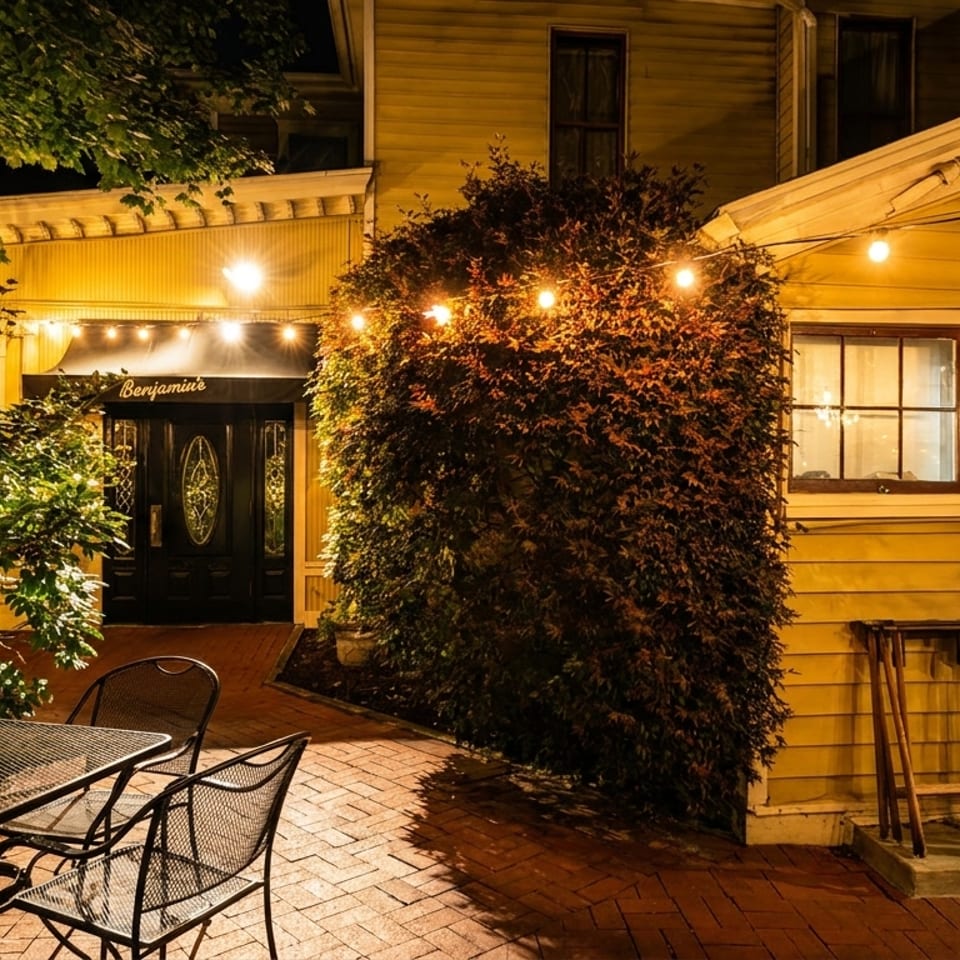 Benjamin's restaurant exterior at night, with string lights, outdoor seating, and a brick patio.