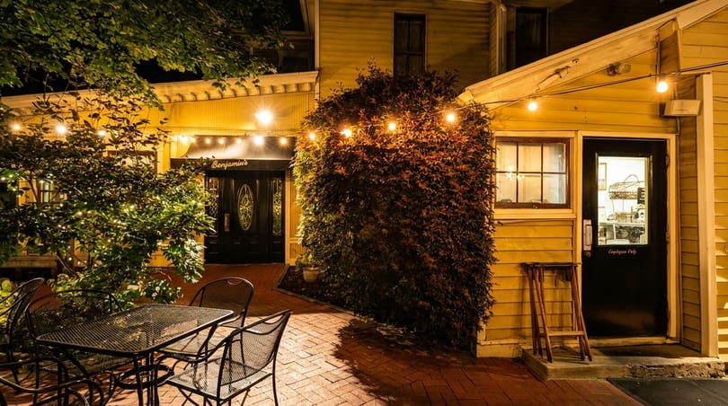 Benjamin's restaurant exterior at night, with string lights, outdoor seating, and a brick patio.