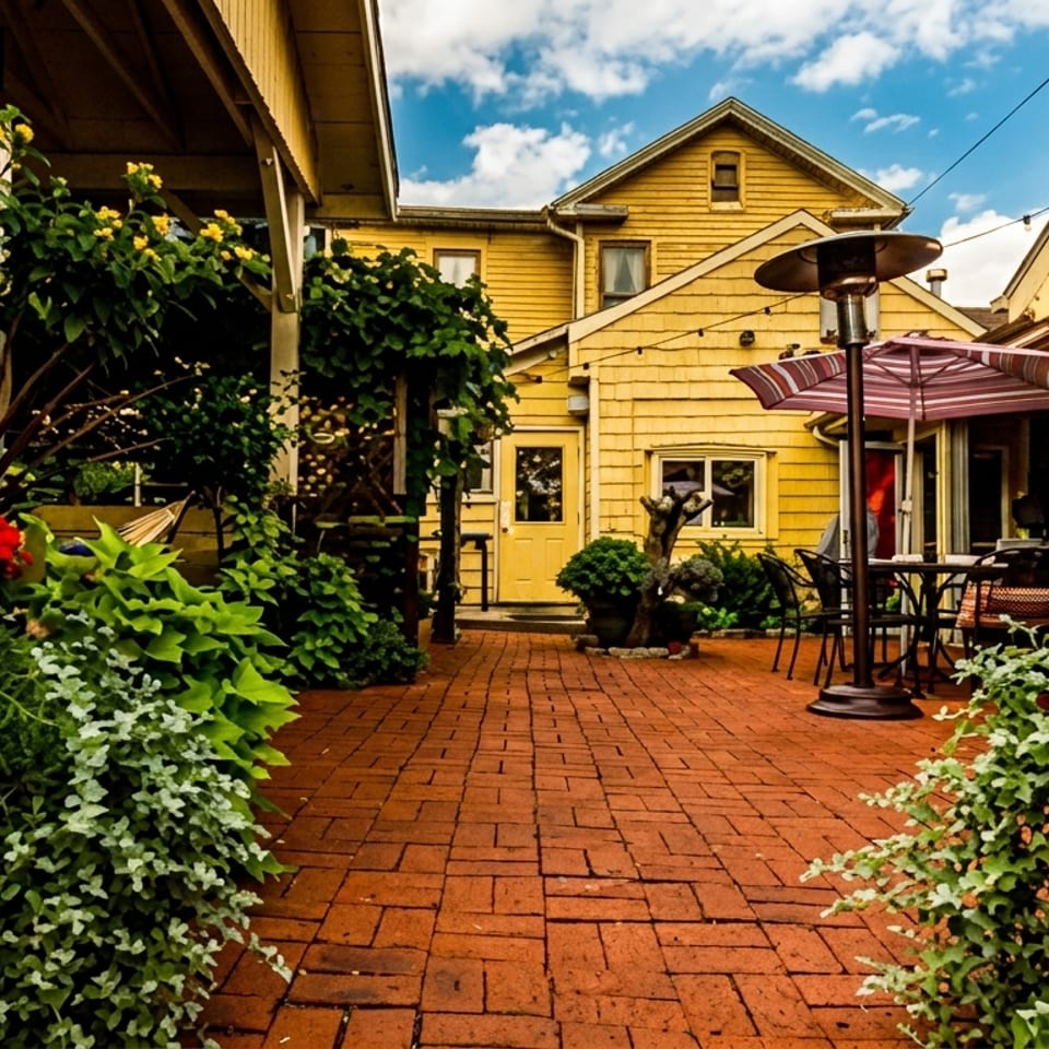 A charming outdoor patio with brick pavers, yellow buildings, and vibrant red and yellow flowers in planters.